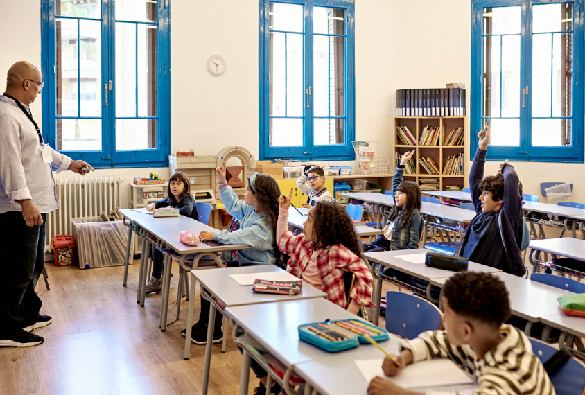 A multiracial group of schoolchildren sit at their desks in class.