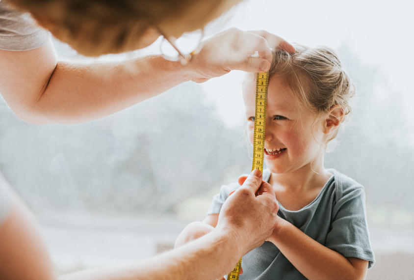 A young girl has her face measured with a tape measure.
