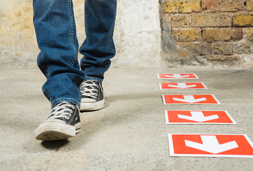 A person wearing blue jeans and black sneakers walks next to a series of arrows placed on the ground.
