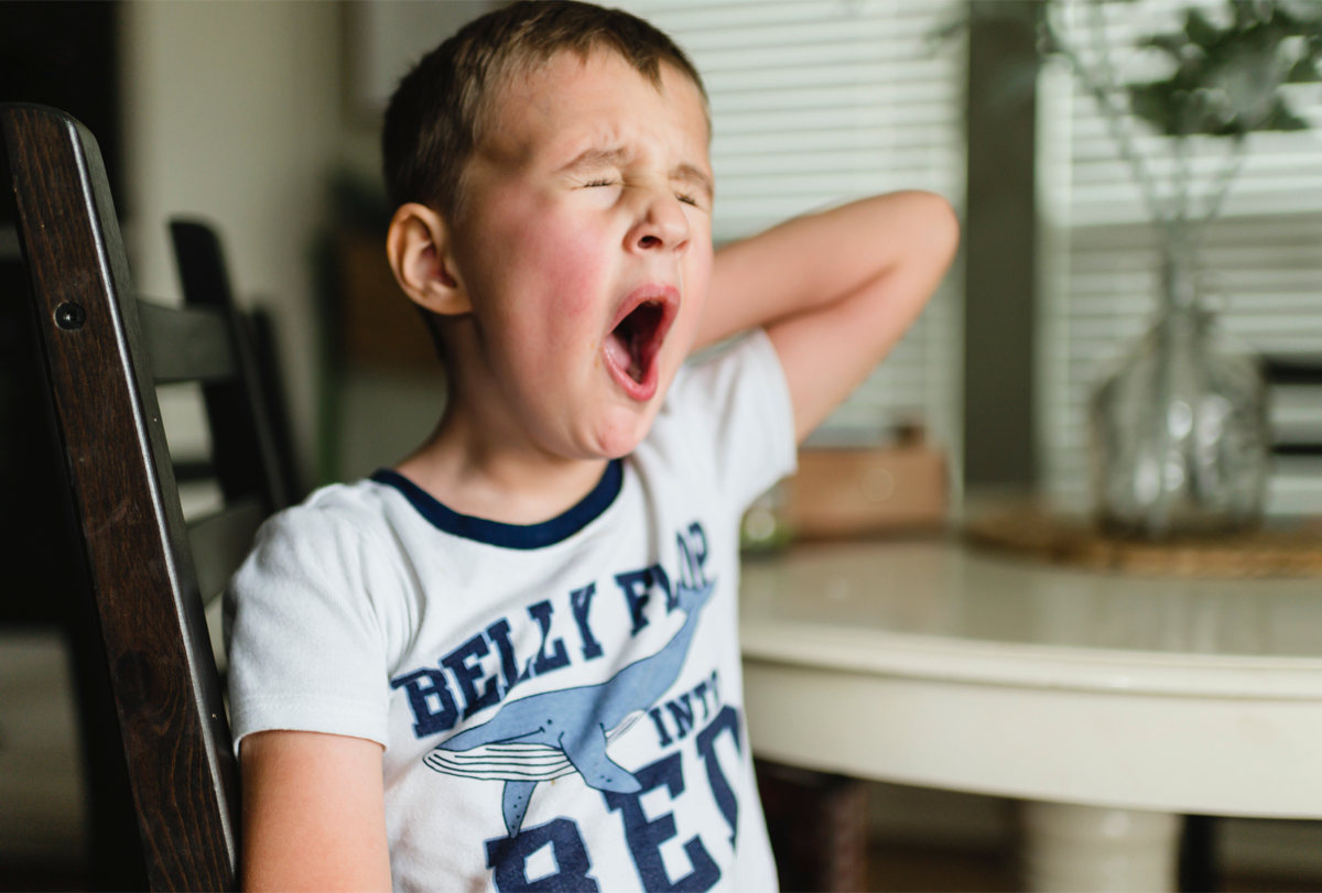Photograph of a child sitting in a chair and yawning.