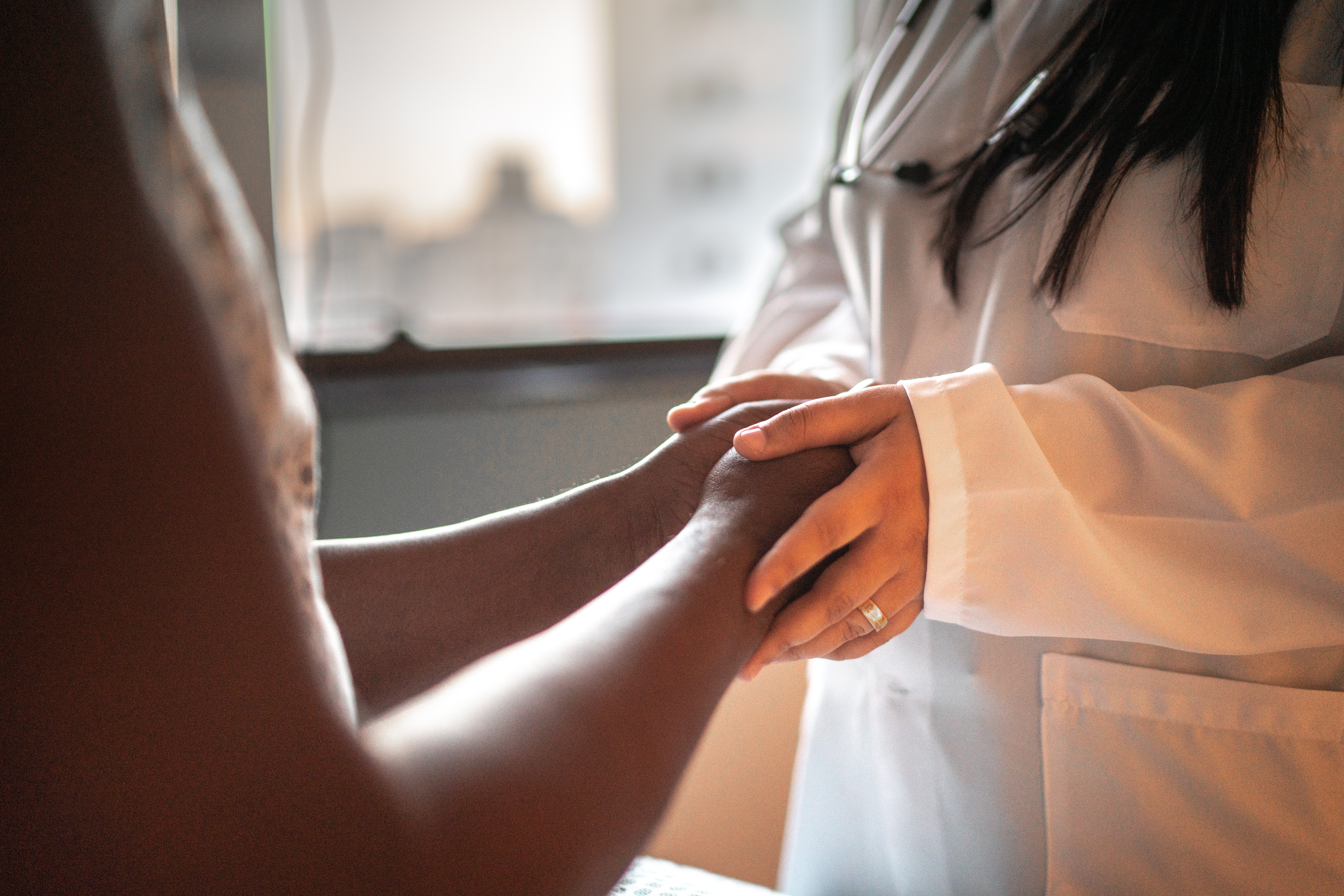 Medical professional in a white coat clasping the hands of a patient.