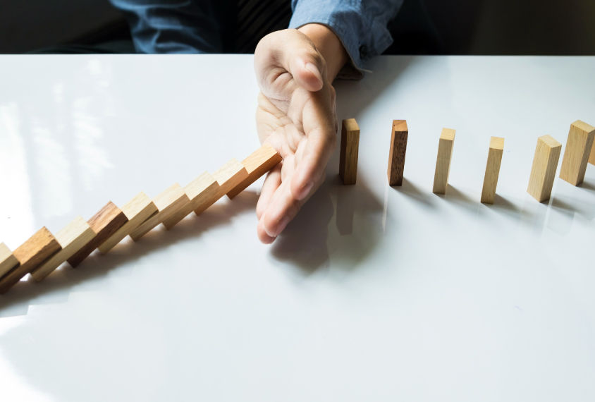 Hand stopping a row of dominoes from collapsing.