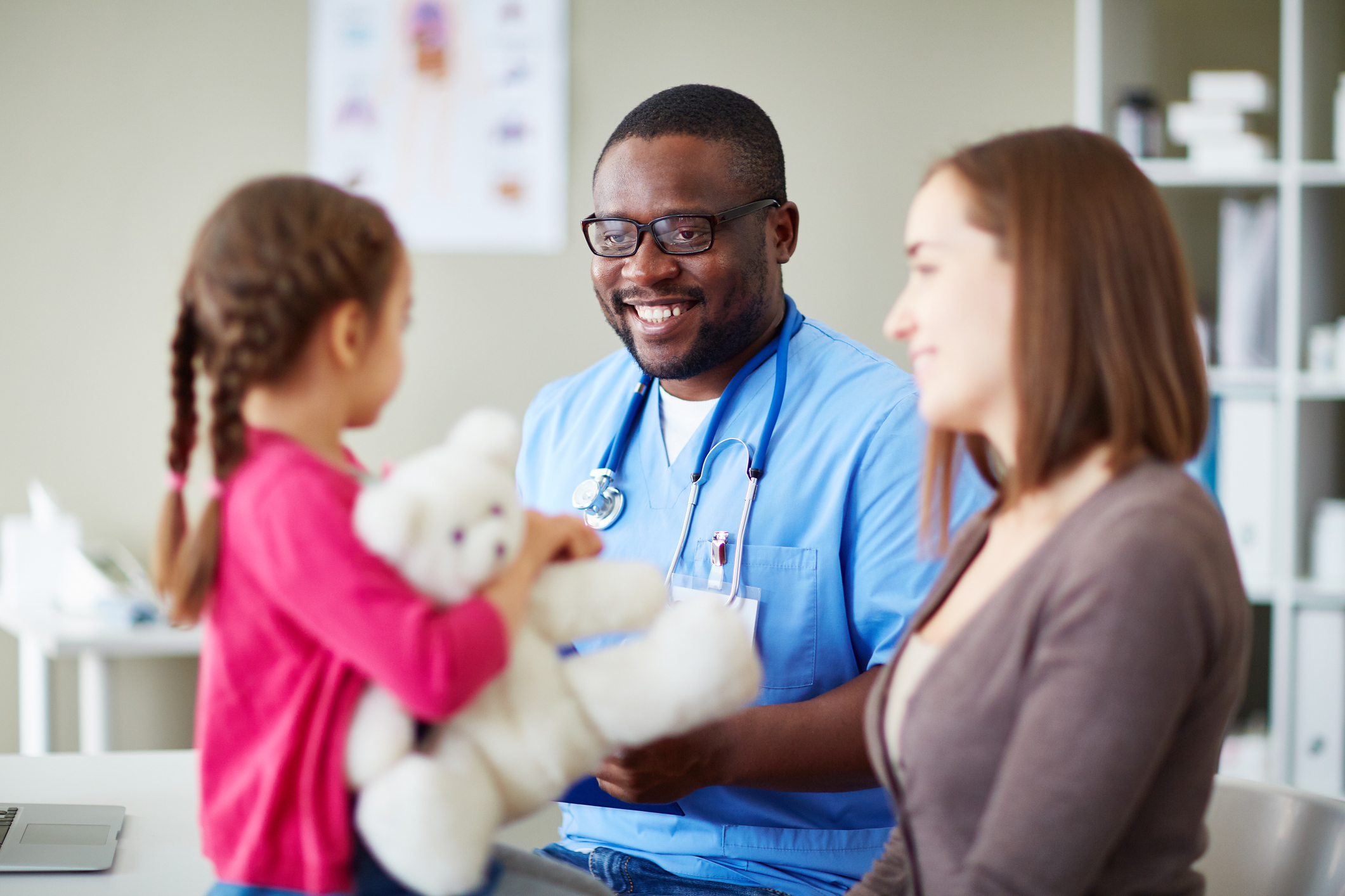 Doctor talking to mom and her daughter, who is holding a teddy bear.