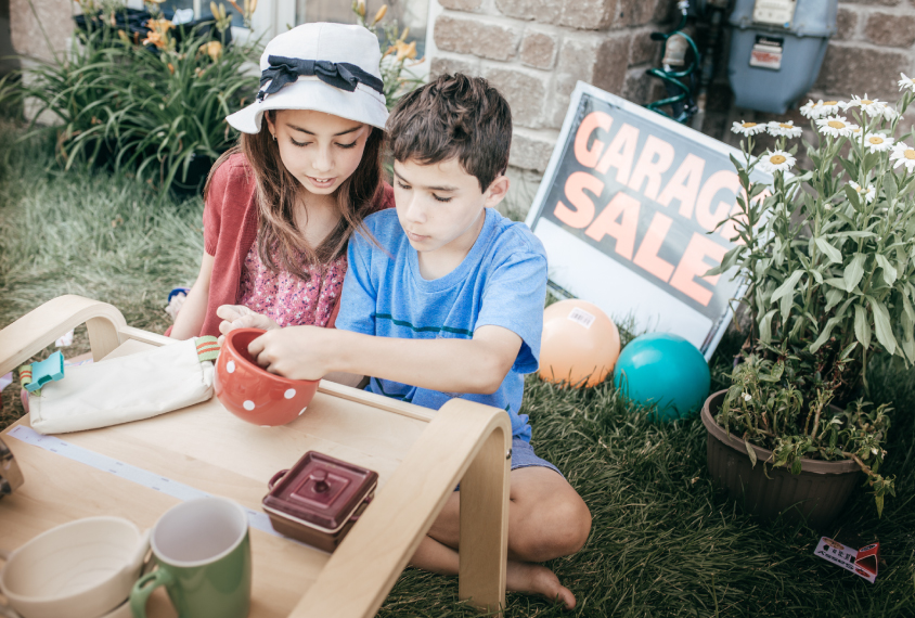 Two children sitting at a garage sale table.
