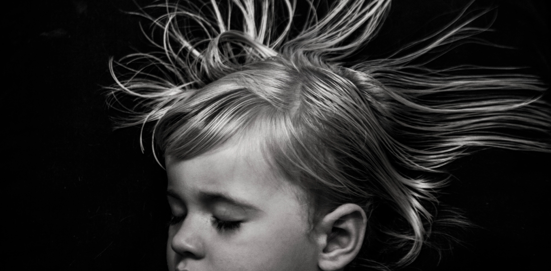 Toddler girl sleeping with hair floating against black background.