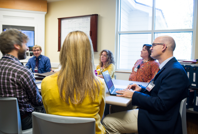 Photo: A team of social workers, therapists, and teachers sit around a grey conference table.