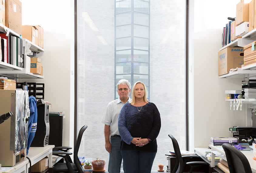 Photo: Bolen stands with Patrick Hof, both looking serious, in Hof's office. Bolen is wearing a blue long-sleeved shirt and jeans. Hof is wearing a white polo and jeans.