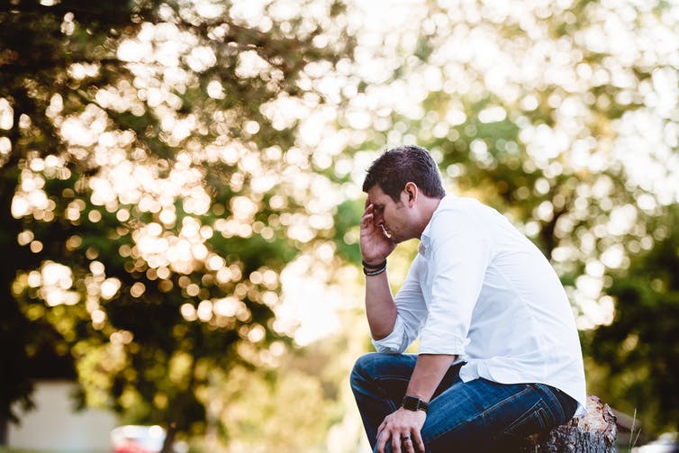 man covering his face while sitting by trees