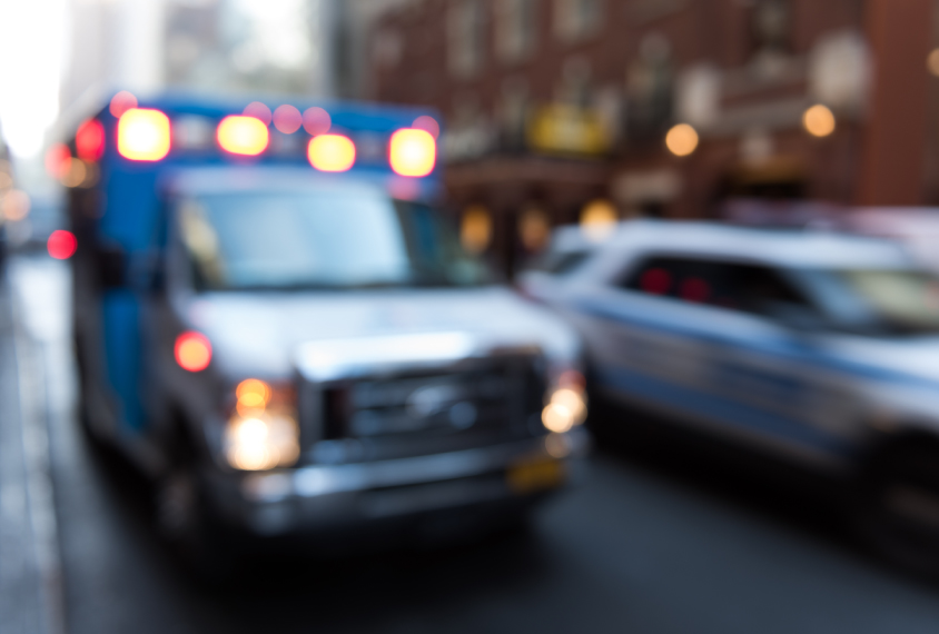 An ambulance and a police car on a city street, lights on.