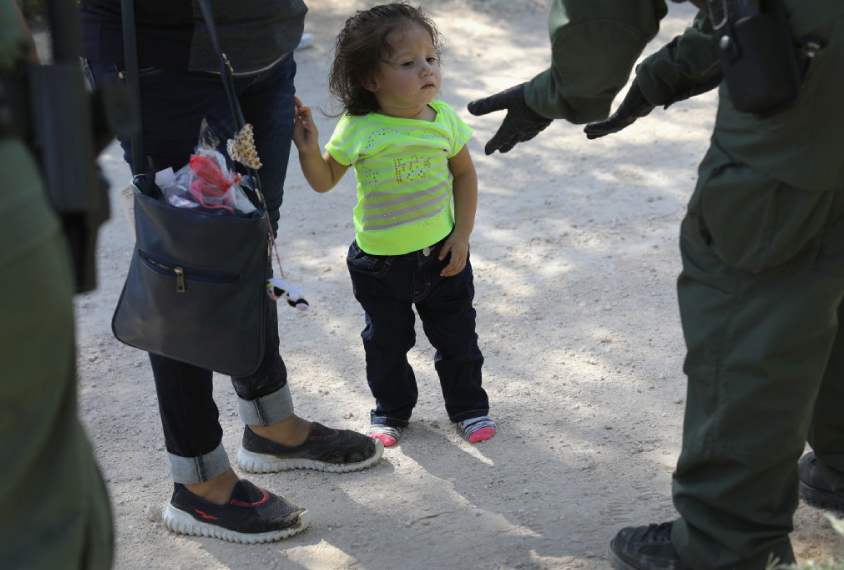 U.S. Border Patrol agents take Central American asylum seekers into custody on June 12, 2018 near McAllen, Texas. A child looks uncertainly at an agent wearing black gloves.