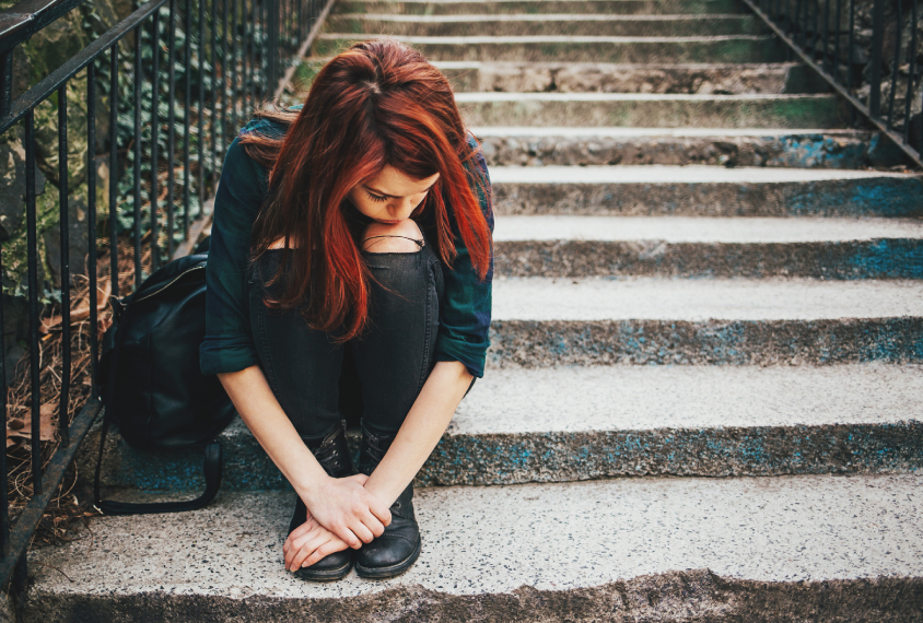 Teen girl sits on stairs, alone, downcast.