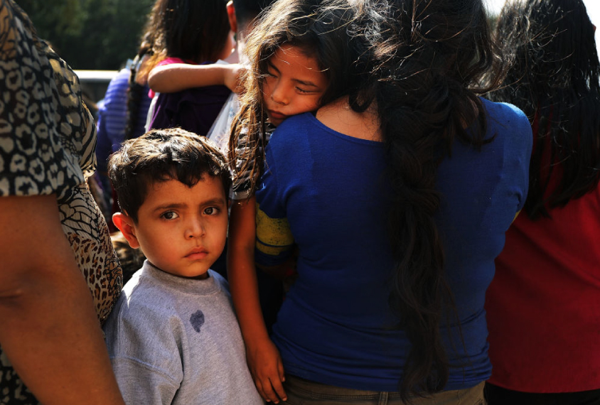 A young boy in crowd of exhausted people looks directly into camera.