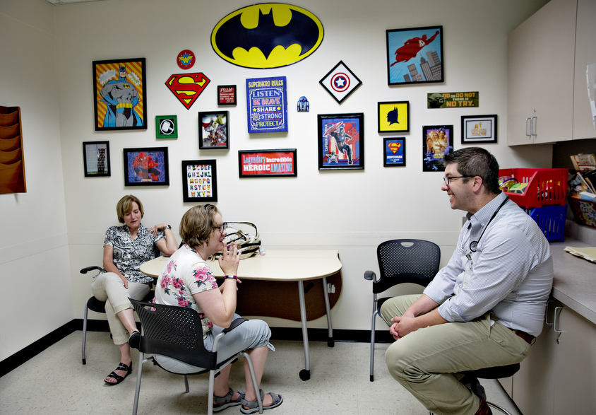 Photo: Two women are sitting around a table, talking to a doctor in his office. One woman has autism and the other is her family member.