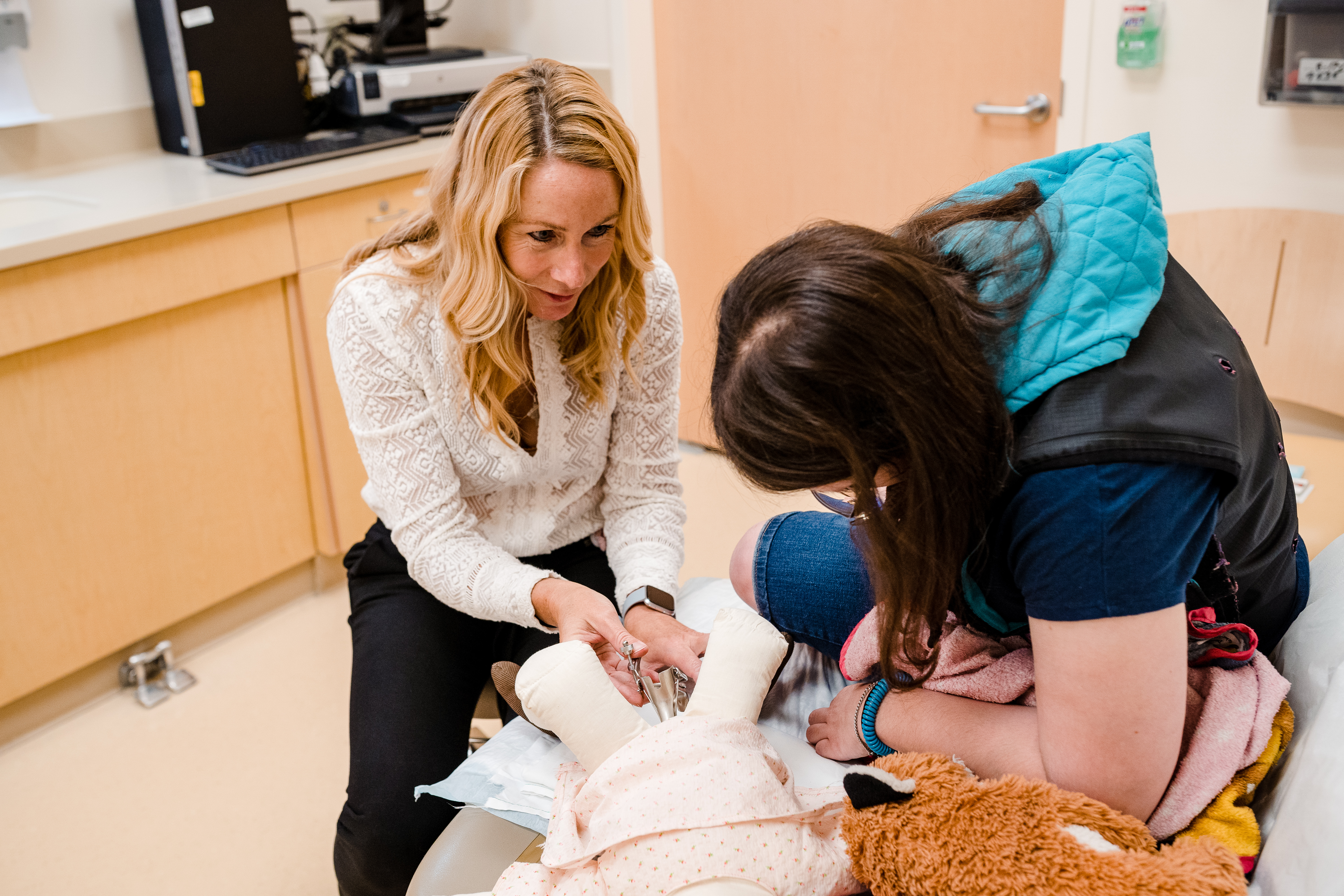 Photo: A gynecologist demonstrates on a doll how a speculum works. A woman with autism watches the demonstration.