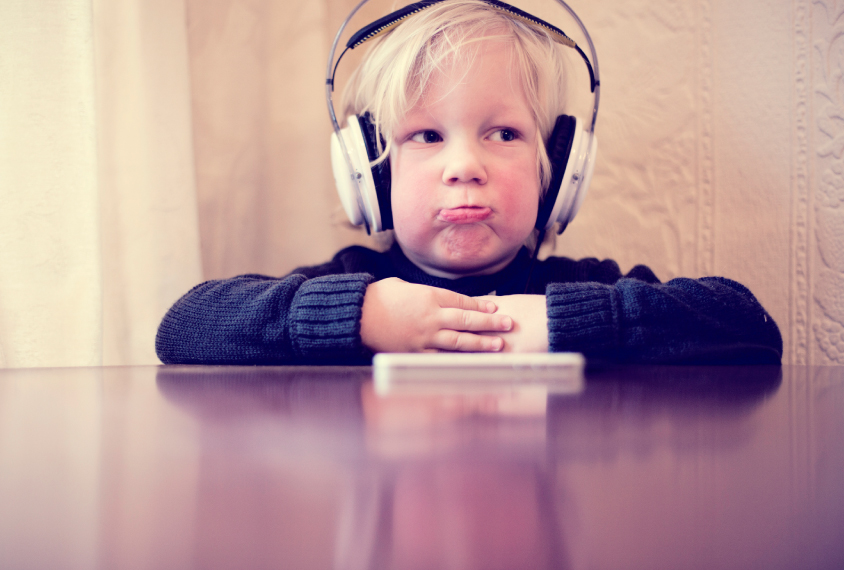 Little boy with headphones on sits at a table, making a funny face.