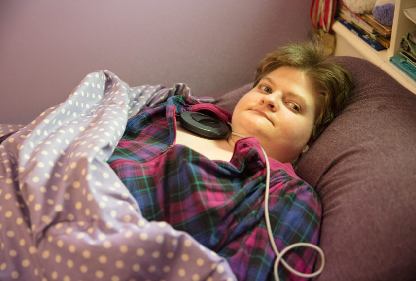 Photo: Autistic woman Becky Audette lies on a couch under a purple blanket.