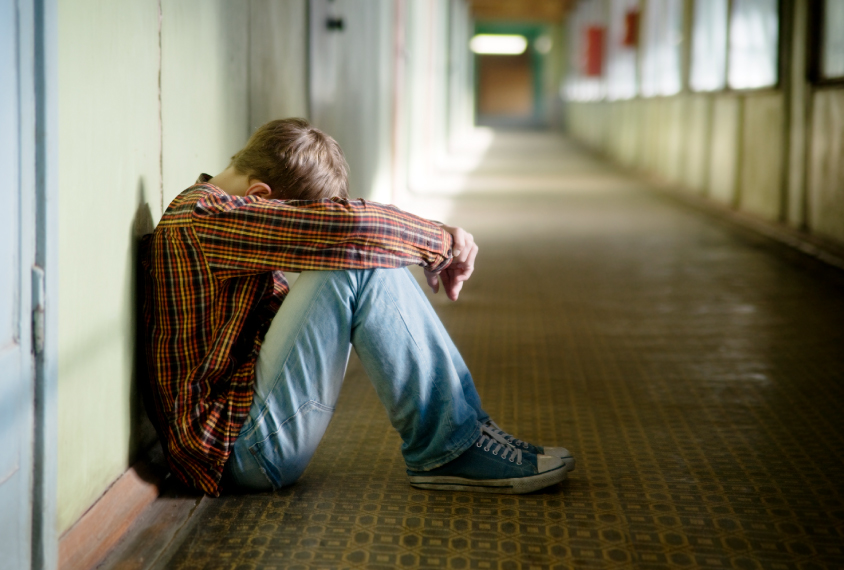 Teenager in hallway, sitting alone with head on knees.