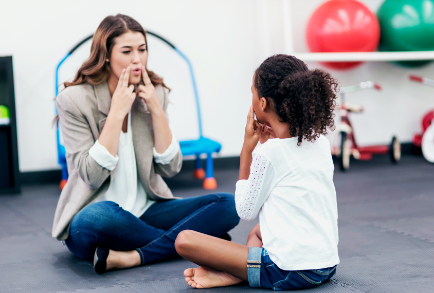 Young girl with teacher in a speech therapy session.