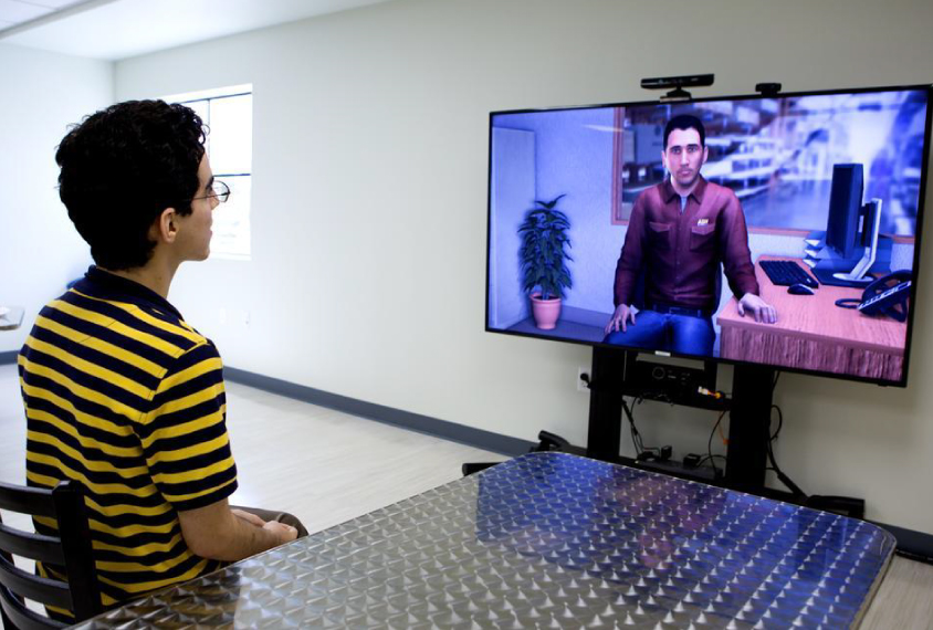 Young man practicing interviewing skills with an avatar on a big screen.