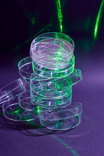 Empty petri dishes in a stack, with a green light shining on them.