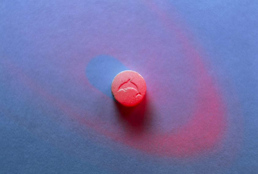 A single ecstasy pill on a blue background.