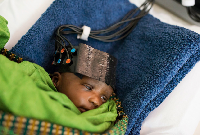 Infant in fnirs cap, wrapped in blankets.