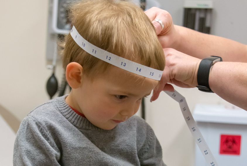 Toddle boy having his head measured in a medical setting.
