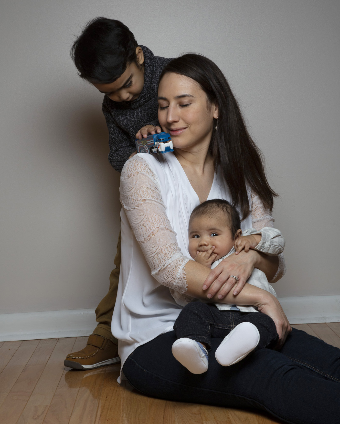 Photo: Melissa Patao sits on the floor, holding an infant. A small child, Shane, stands over her shoulder, playing with a toy bus.