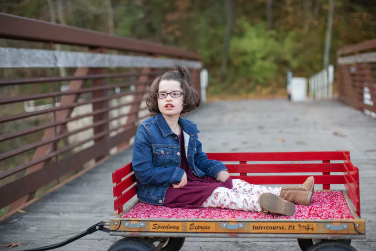 Child with Pitt-Hopkins syndrome seated in a red wagon outside.