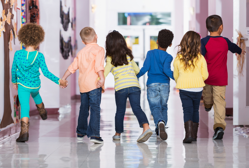 A group of boys and girls holding hands walking on a school hallway