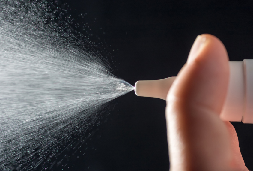 Nasal spray jetting from bottle on a dark background