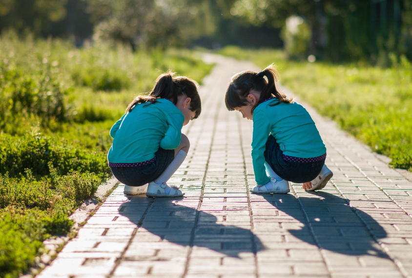 Two twin girls wearing blue kneeling down on the ground.