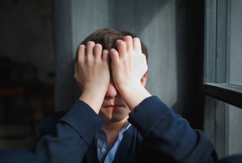 Young man sits alone with his hands over his face