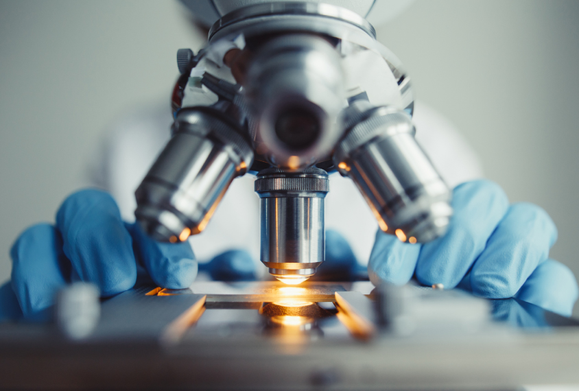 close up of microscope and researcher's gloved hands