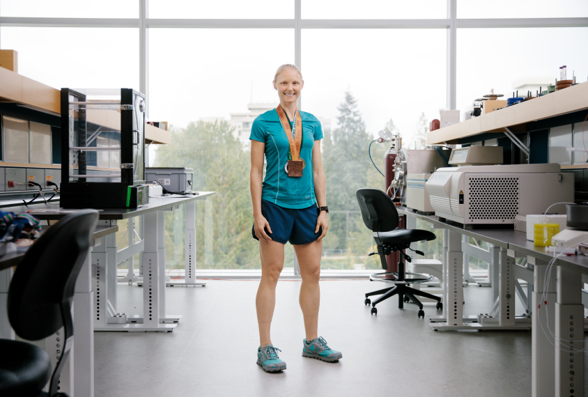 Scientist Annie Ciernia standing in her lab, wearing her running gear and medals. 
