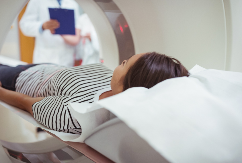 Woman inside MRI machine with clinicians or doctors looking on with clipboards