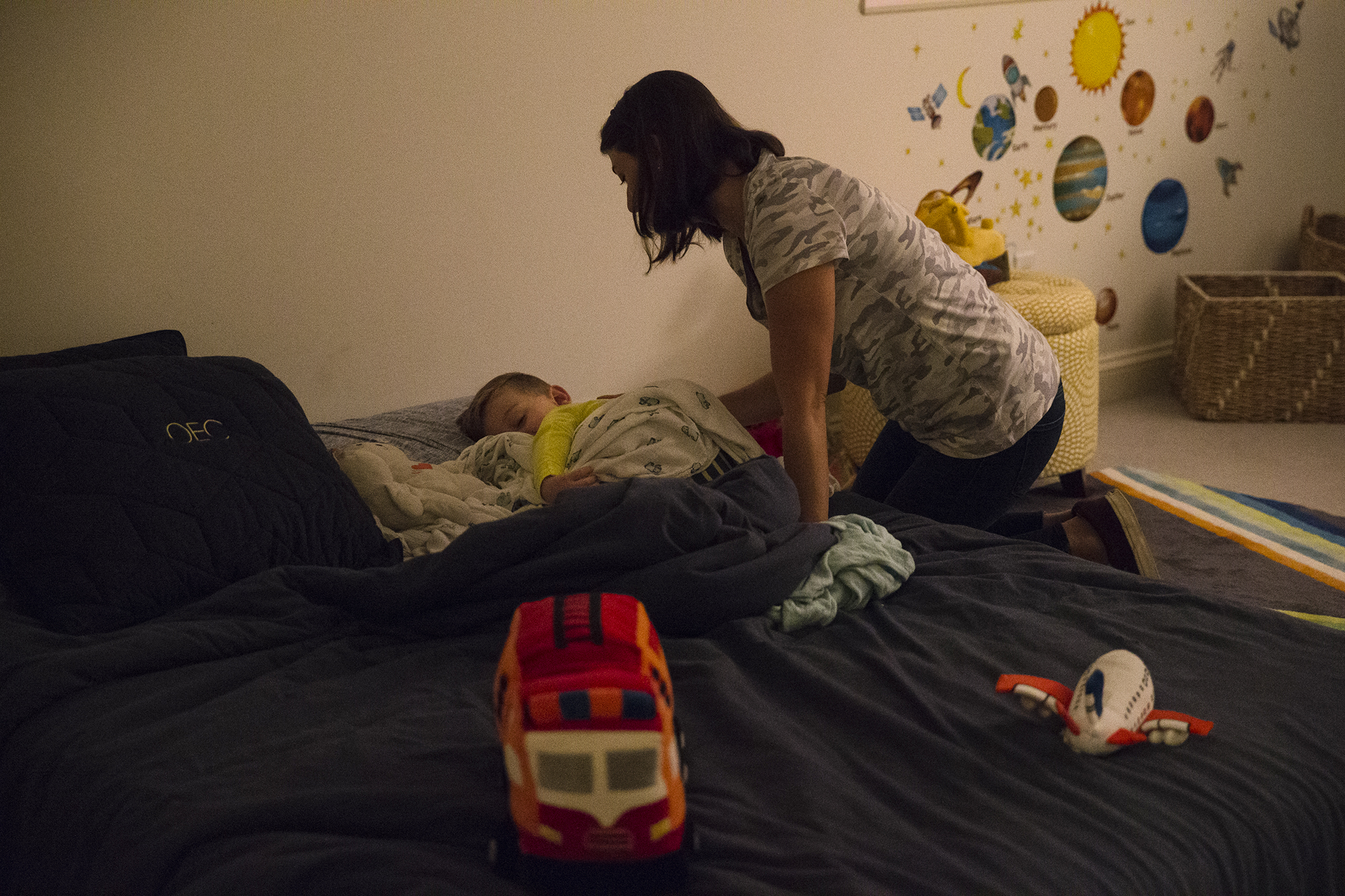 Photo: A mother leans over a bed to look at her sleeping child.
