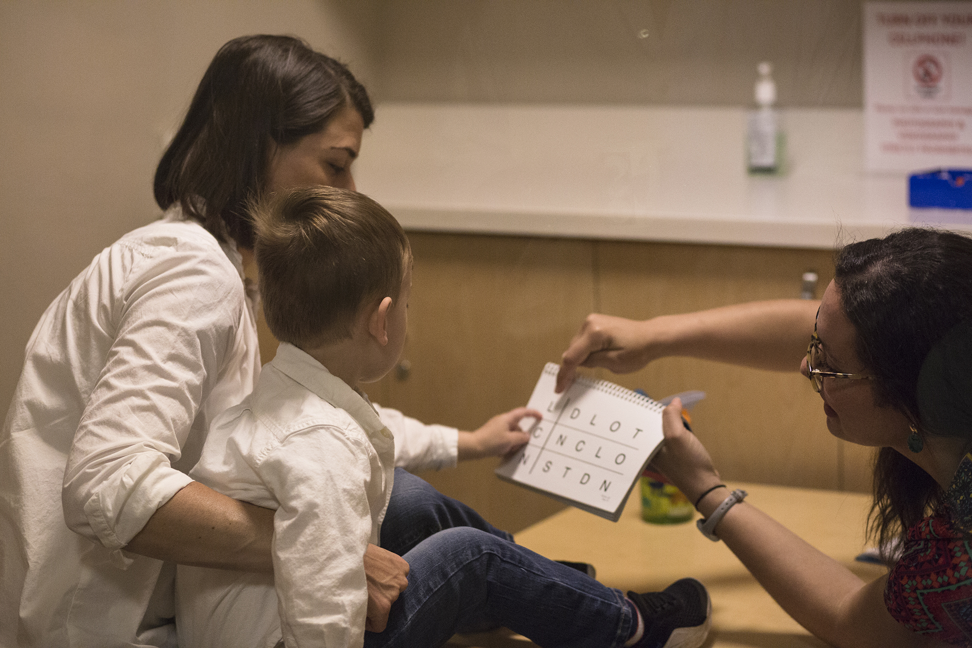 Photo: Owen sits on his mother's lap looking at a workbook held up by a physician.