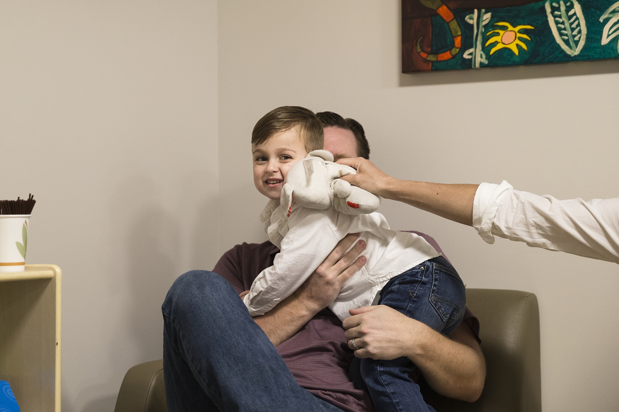 Photo: Owen sits on his father's lap in the doctor's office. Owen's mother's arm is in the frame holding Owen's stuffed toy.