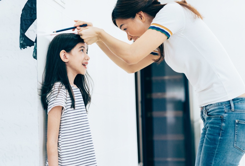 a young girl has her height measured by a woman