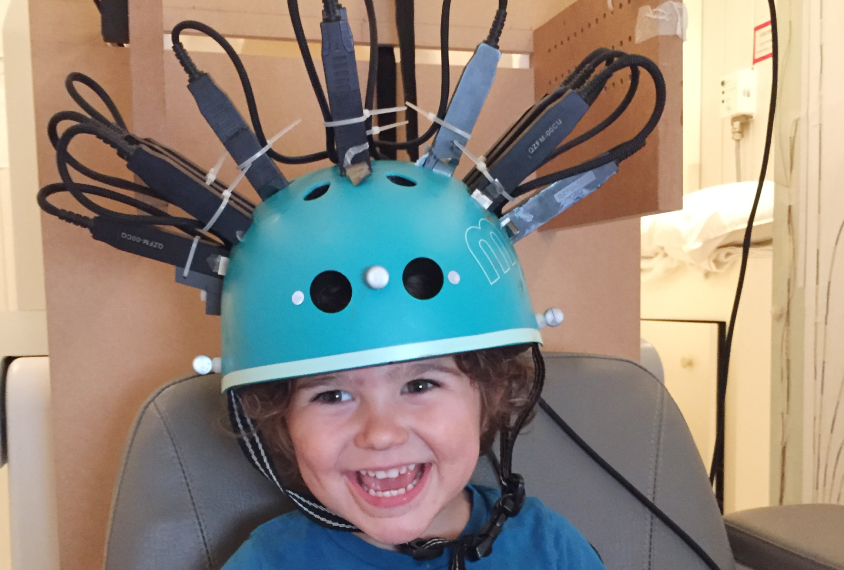 Child in a bike helmet repurposed as a brain scanner, smiles and laughs