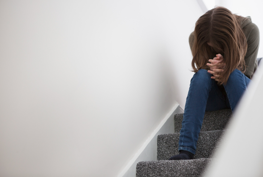 A young teen woman sits on stairs with her head hanging down, her face hidden by her hair.