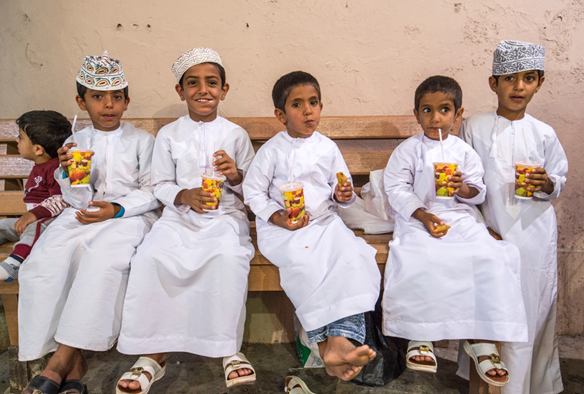 Young boys in Oman in a market sit and drink juice