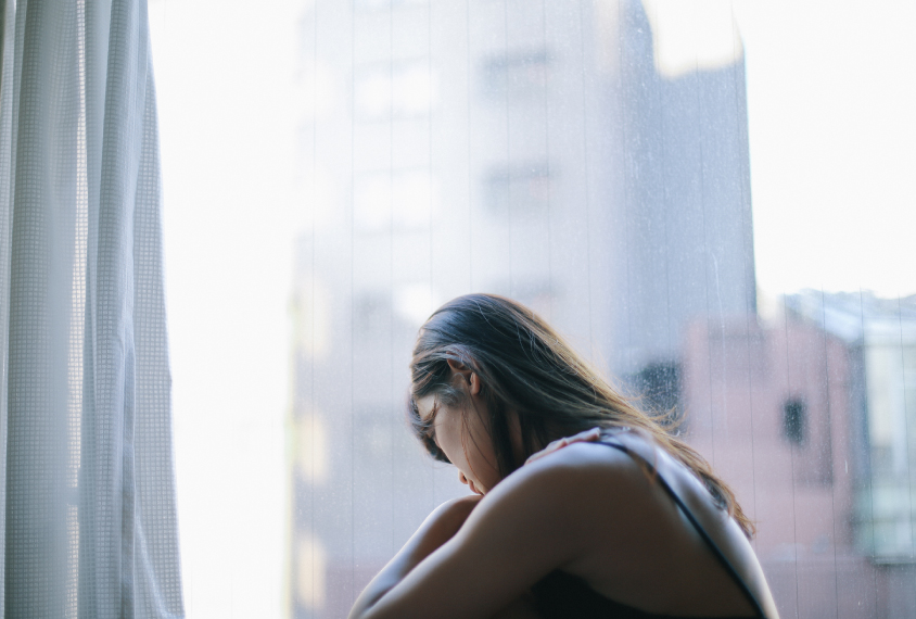 Teenage girl sad and sitting by window.