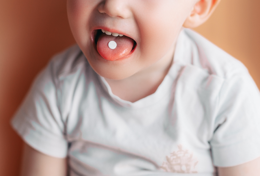 Small child with pill in mouth.