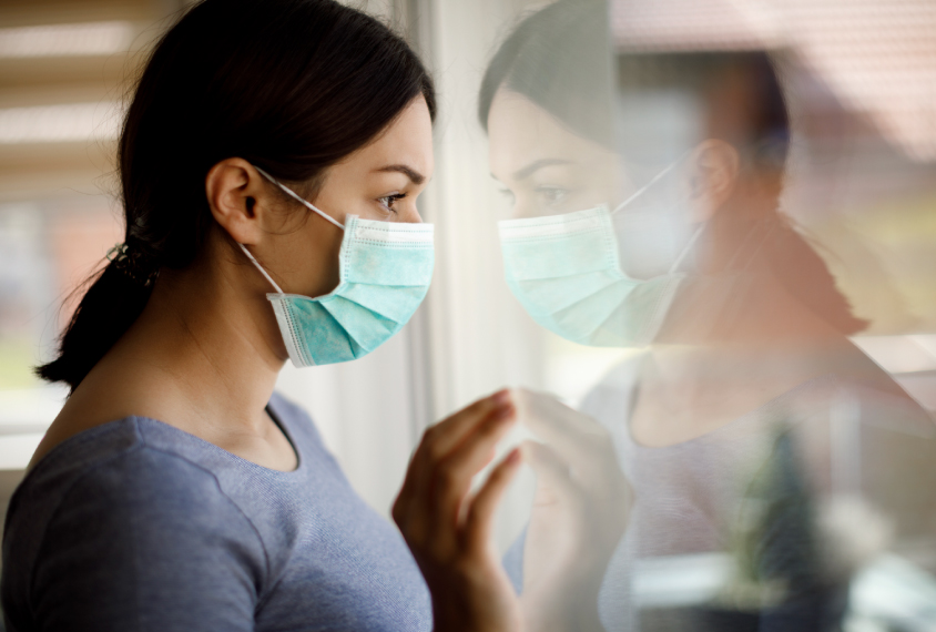 A young woman wearing a face mask looks out the window