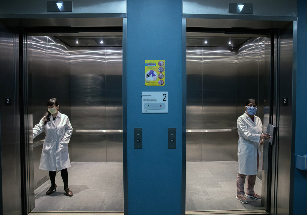 two researchers in two separate elevators, wearing COVID-19 protective gear