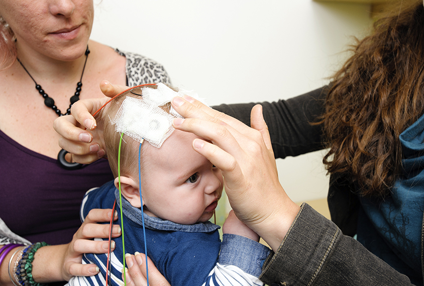 Researcher attaching electrodes to a baby's head during an electroencephalography study in the Sleep Room