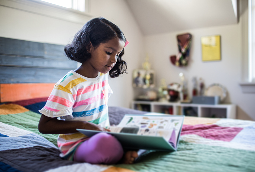 Young child on her bed looking at a book.