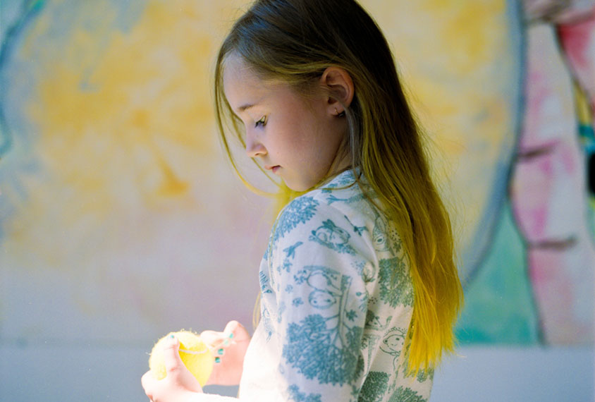 young autistic girl in playroom with a tennis ball that matches her yellow dyed hair.